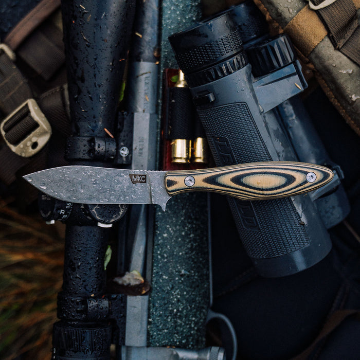 JACKSTONE knife in tan and black with a patterned handle, resting on a textured surface among outdoor gear.