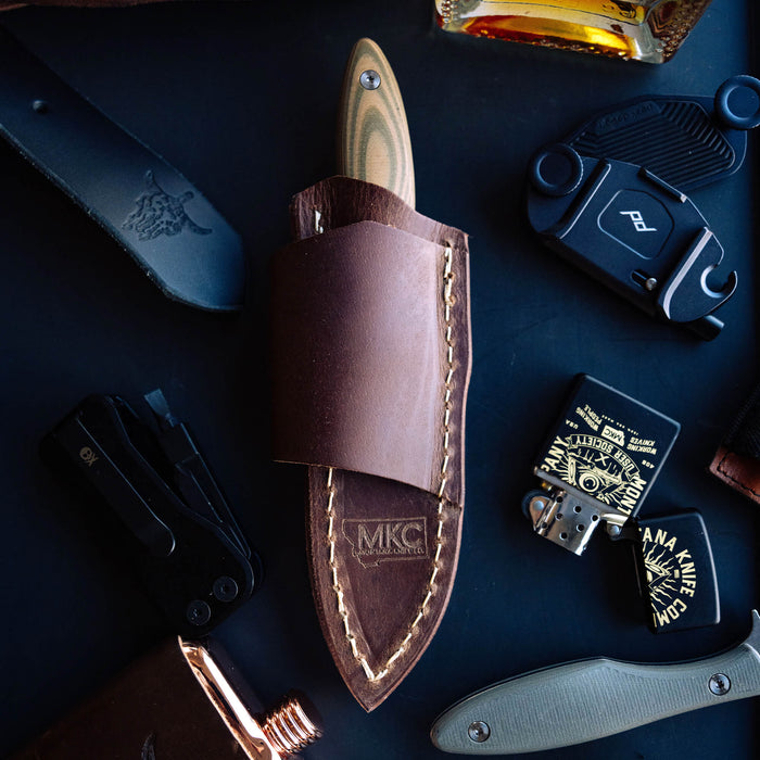 Horizontal leather sheath for Jackstone knife, featuring durable stitching and MKC branding, surrounded by EDC gear.