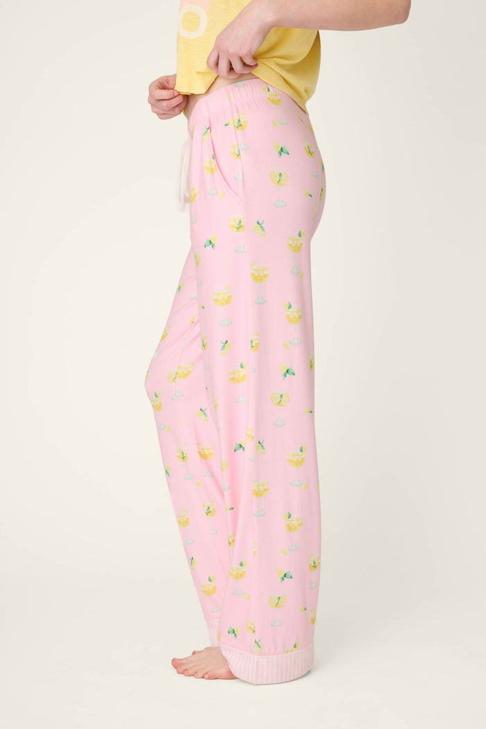 A person in P.J. Salvage's La Dolce Spritz Limoncello Life Pajama Pants and a yellow T-shirt stands barefoot in profile against a plain light background.