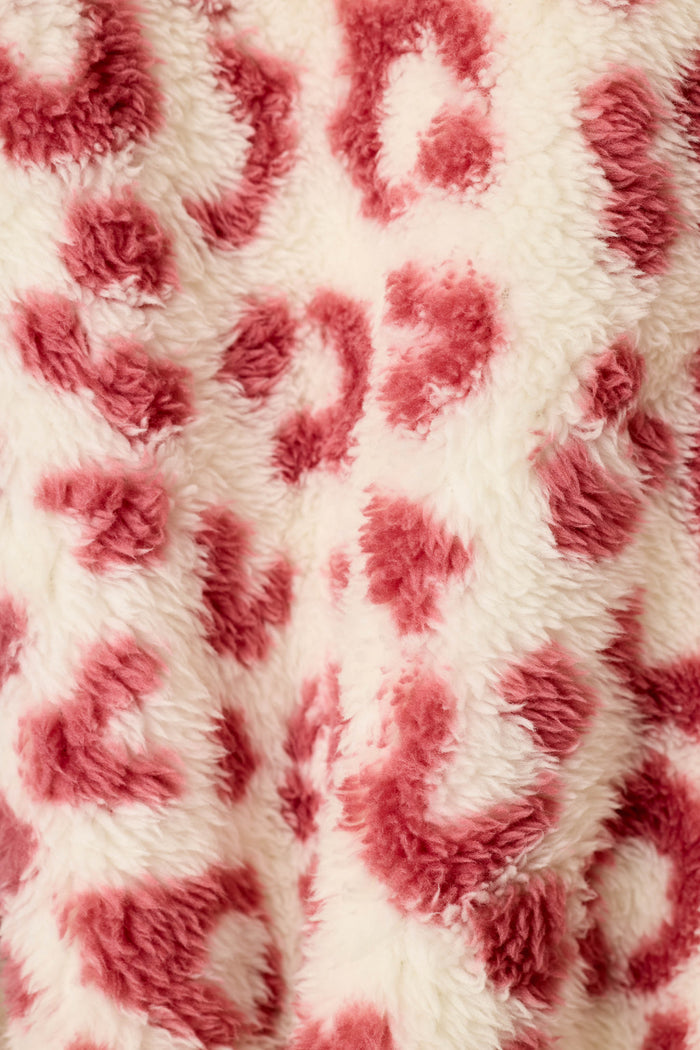 Close-up of a plush faux-fur fabric with a dusty wine leopard print pattern on a cream ground.