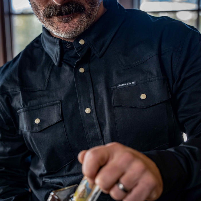 A man wearing a black long sleeve pearl snap shirt with two front pockets, showcasing a rugged style suitable for outdoor activities.