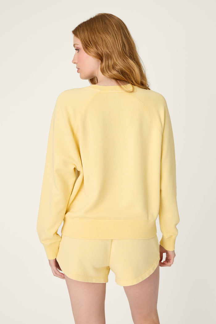 A person with long, light brown hair faces away from the camera, wearing a pastel yellow sweater against a plain light background.