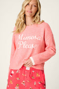 A woman with long blonde hair wears the P.J. Salvage Mimosa Please Snuggle Sweater in pink, featuring “Mimosa Please” in white lettering, paired with matching pink pajama pants decorated with playful cartoon brunch food and drink prints.