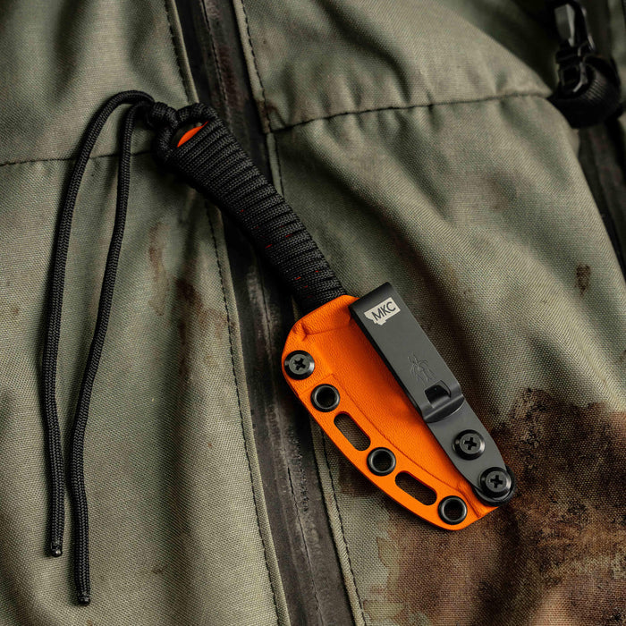 MINI SPEEDGOAT 2.0 knife in an orange Kydex sheath, secured to a textured fabric background, showcasing its tactical design.