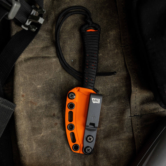 Mini Speedgoat 2.0 knife with orange Kydex sheath, resting on a rugged fabric surface, showcasing its compact design.