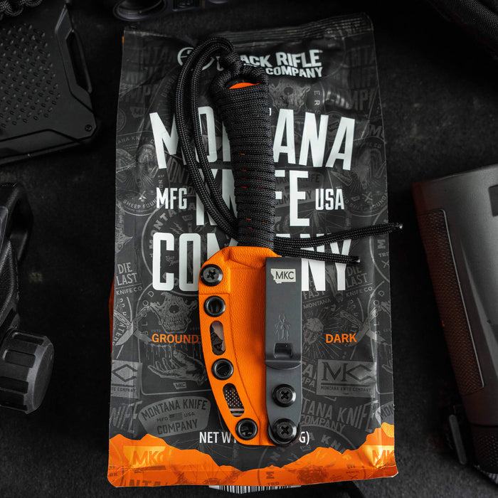 MINI SPEEDGOAT 2.0 knife with orange handle and Kydex sheath, displayed on a branded Montana Knife Company background.