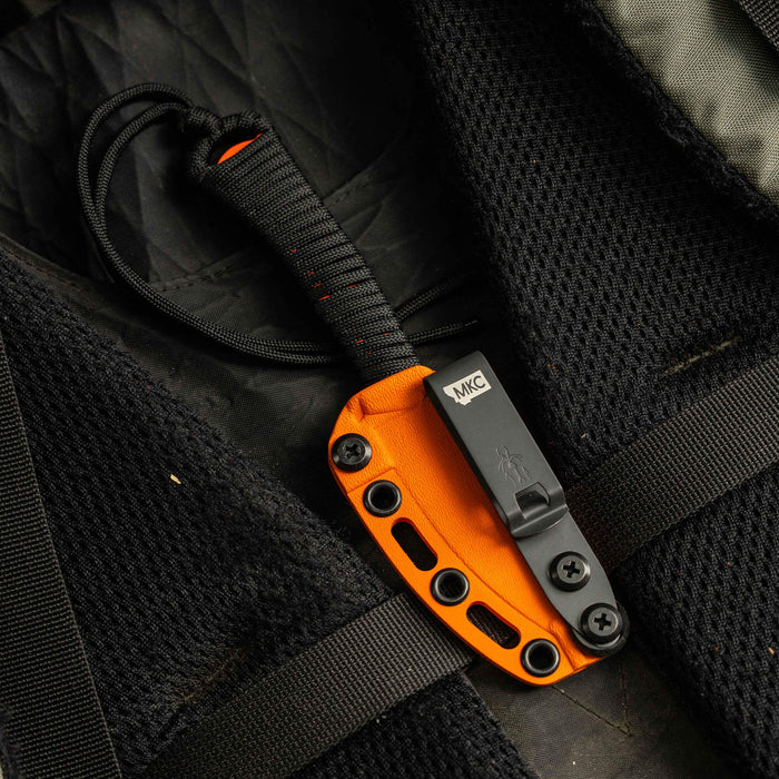 MINI SPEEDGOAT 2.0 knife with additional Kydex sheath, featuring an orange handle and secure attachment on a backpack.