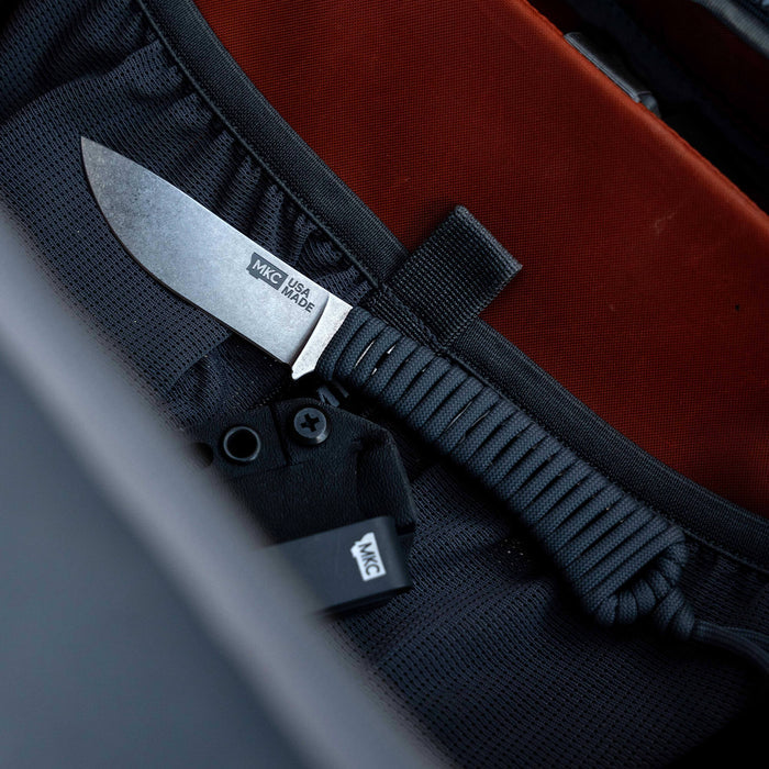 Mini Stoned Goat knife in black resting in a backpack pocket, showcasing its compact design and durable blade.