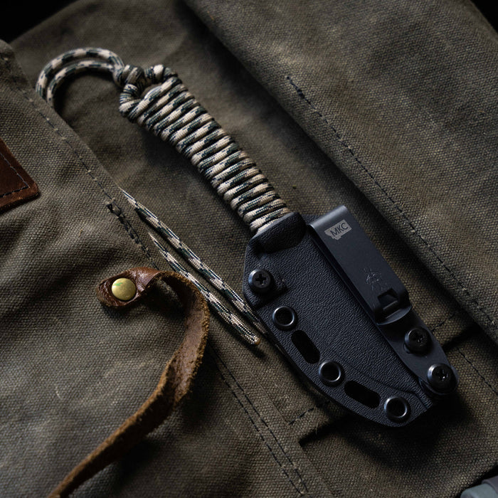 Mini Stoned Goat knife in desert camo with a paracord handle, resting on a rugged canvas background.