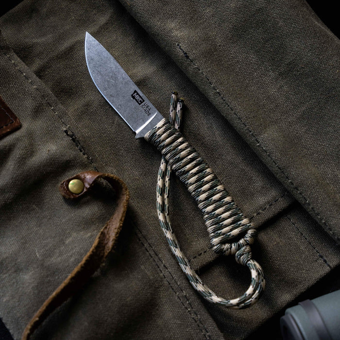 Mini Stoned Goat knife in desert camo with paracord handle, resting on a rugged canvas background.
