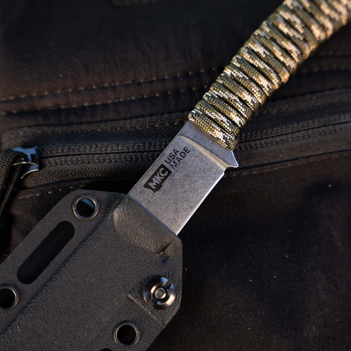 Close-up of the MINI STONED GOAT knife in forest camo, showcasing its blade and textured handle for grip.