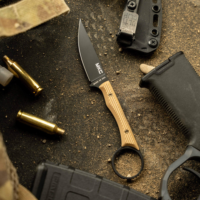 MINI WARGOAT knife with a black blade and gold handle, surrounded by tactical gear and ammunition on a sandy surface.