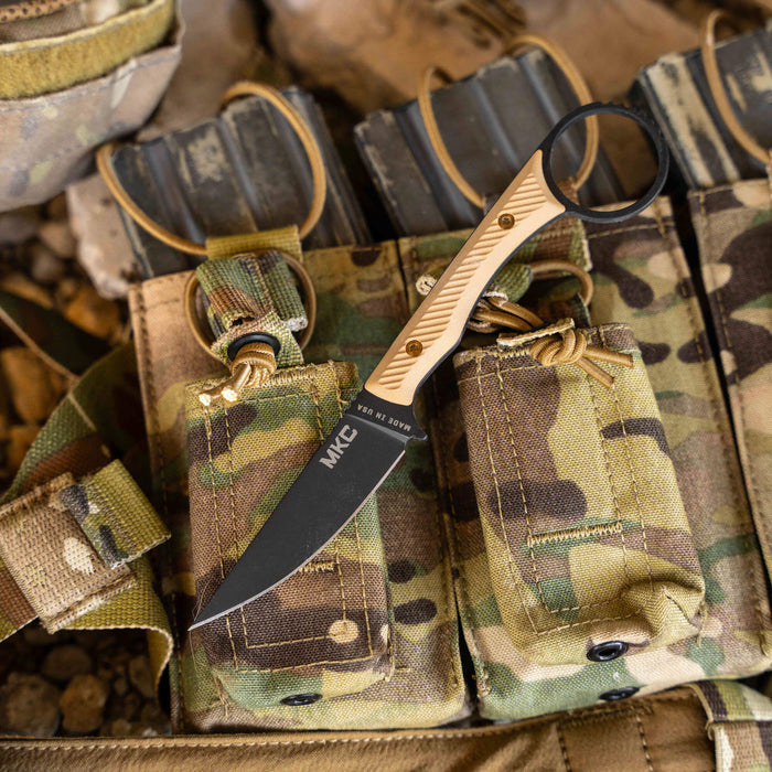 MINI WARGOAT knife with a black blade and tan handle resting on camouflaged tactical gear.