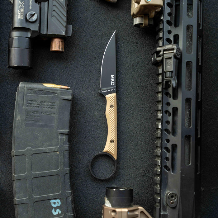 MINI WARGOAT knife with a black blade and tan handle, surrounded by tactical gear and accessories.