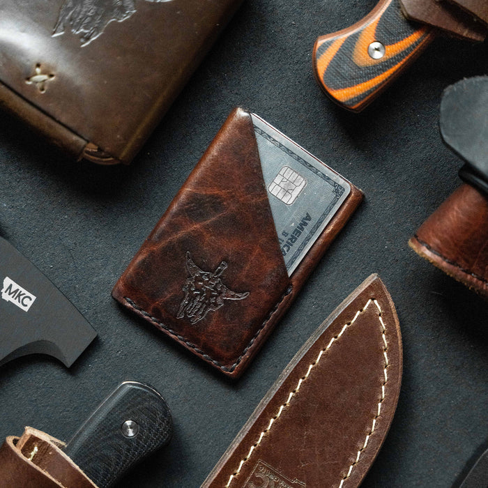 Mini leather wallet featuring a bison skull design, surrounded by knives and leather goods on a dark surface.