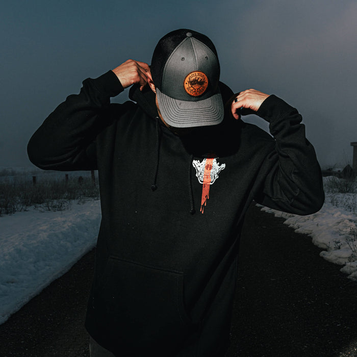 Black MKC Blood Brothers hoodie featuring a graphic design, worn by a person adjusting their hat in a snowy outdoor setting.