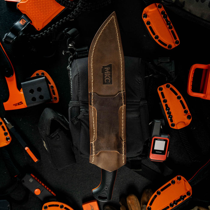 MKC Chopper leather sheath displayed on a black bag, surrounded by orange tactical gear and tools.