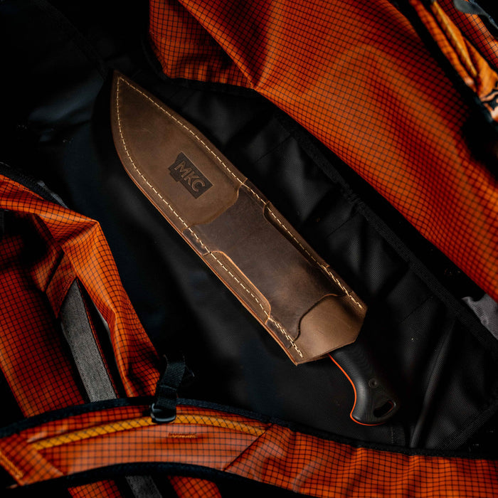 MKC Chopper leather sheath holding a fixed-blade knife, placed inside an orange backpack.