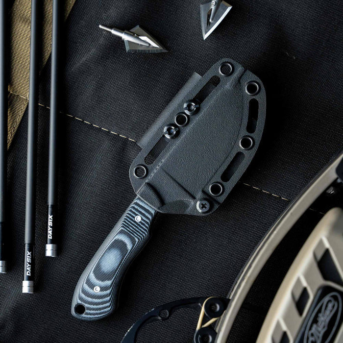 MKC Elk Knife Live Wild Edition in grey and black with sheath, surrounded by hunting gear and tools.