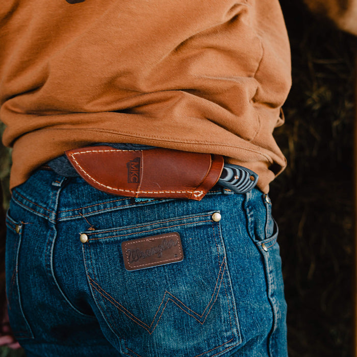 Horizontal leather sheath for MKC Elk Knife, worn on a belt, showcasing rugged outdoor style and practicality.