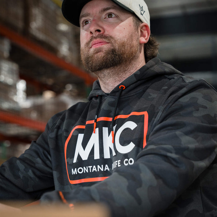 Man wearing a dark woodland camo fleece hoodie with MKC logo, showcasing a rugged style ideal for outdoor activities.