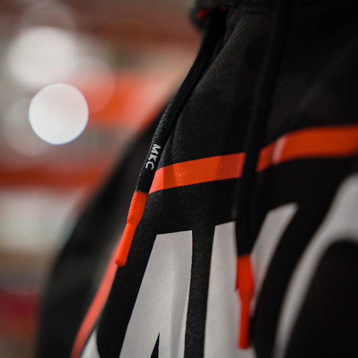 Close-up of MKC fleece hoodie in dark woodland camo featuring bold logo and adjustable drawstrings for outdoor wear.