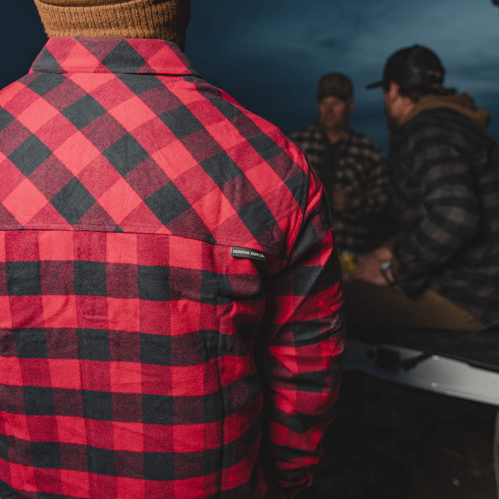 Red and black checkered flannel shirt worn outdoors, with people in the background engaged in conversation.