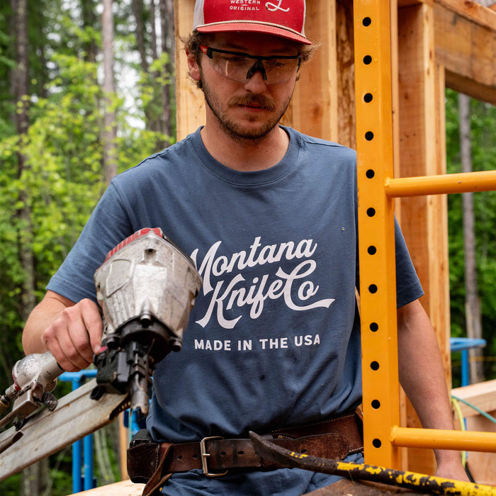 Man wearing a blue Montana Knife Company Heritage Tee, working on a construction site with a nail gun.