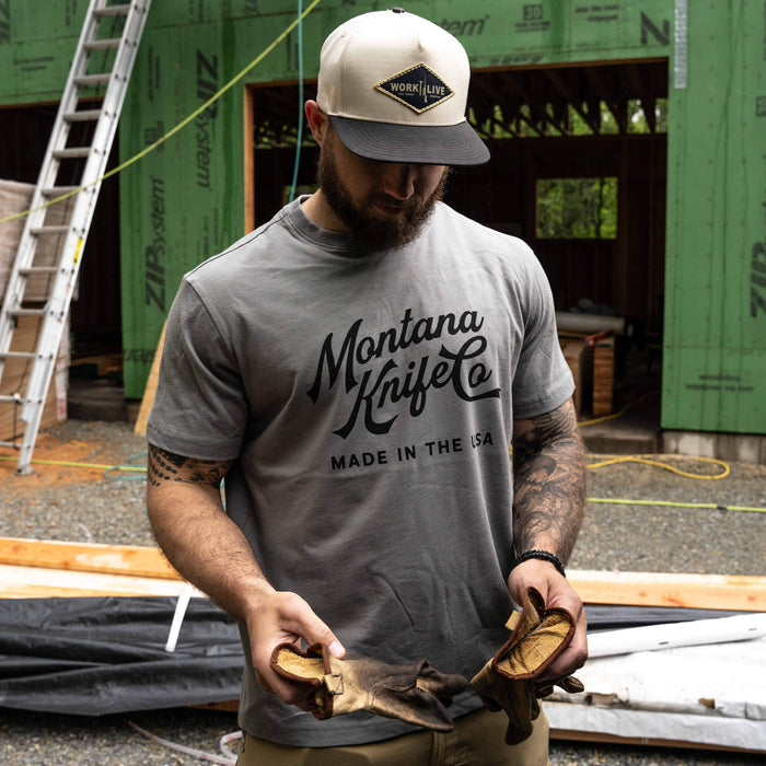 Man wearing a stone-colored MKC Heritage Tee, showcasing the Montana Knife Co logo, in a construction setting.