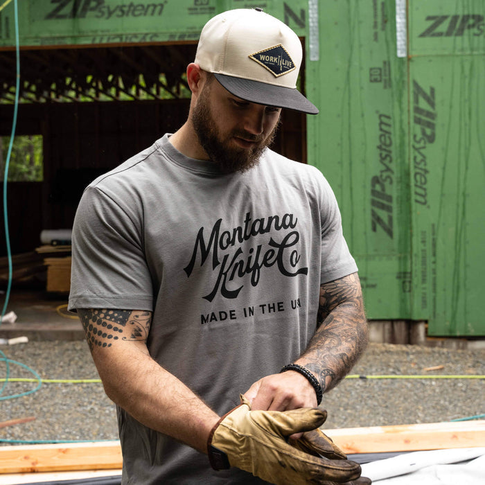 Man wearing a stone-colored MKC Heritage Tee, showcasing the Montana Knife Company logo, in a construction setting.