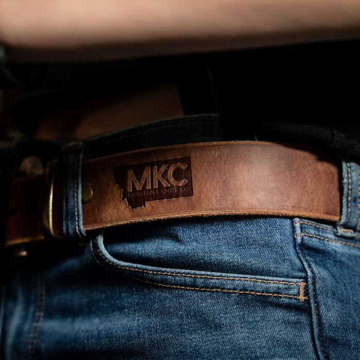Brown leather belt featuring the Montana Knife Company logo, worn with denim jeans, showcasing durability and style.
