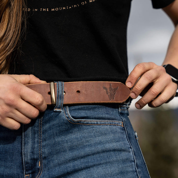 Brown leather belt from Montana Knife Company, featuring a subtle logo, worn with denim jeans and a black shirt.