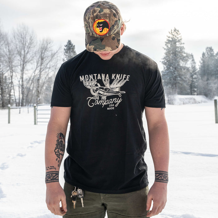 Black MKC Moose Tee featuring the Montana Knife Company logo, worn by a person in a snowy outdoor setting.