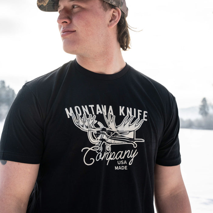 Black MKC Moose Tee featuring a graphic design with antlers and the Montana Knife Company logo, worn by a man outdoors.