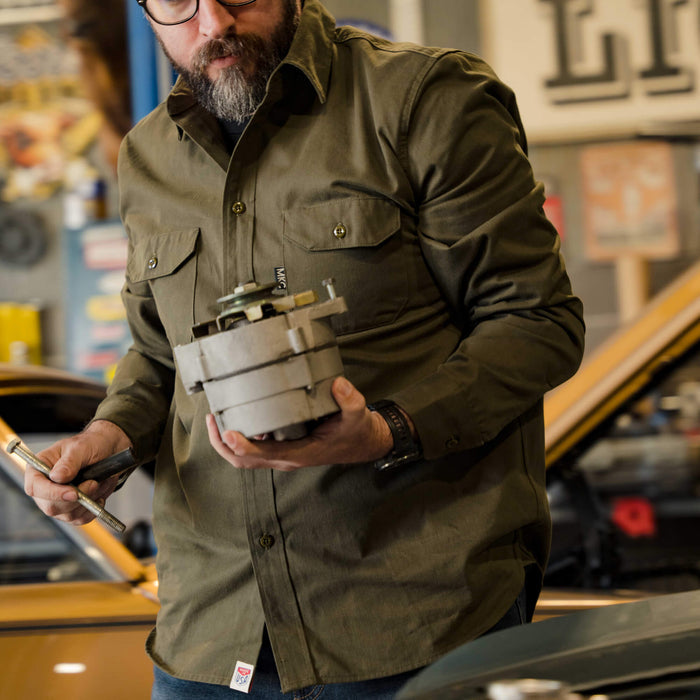 Olive green MKC shop shirt, USA made, worn by a man working on a car engine in a garage setting.