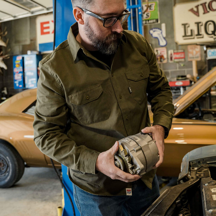 Olive MKC shop shirt being worn by a man working on a car in a garage, showcasing durability and utility.