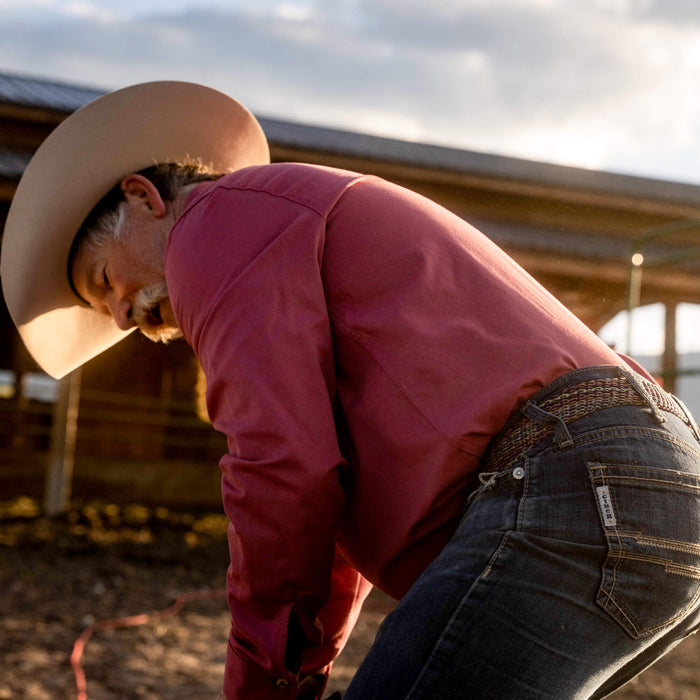 Man wearing a redwood MKC shop shirt, cowboy hat, and jeans, working outdoors on a ranch.