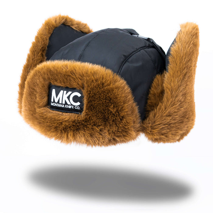 Montana Knife Company Trapper Hat featuring a black exterior and brown faux fur lining, ideal for outdoor activities.