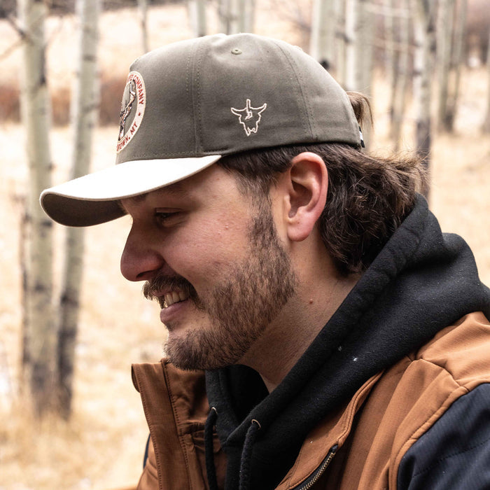 Man wearing MKC Whitetail Hat, featuring a logo, set against a natural outdoor background.