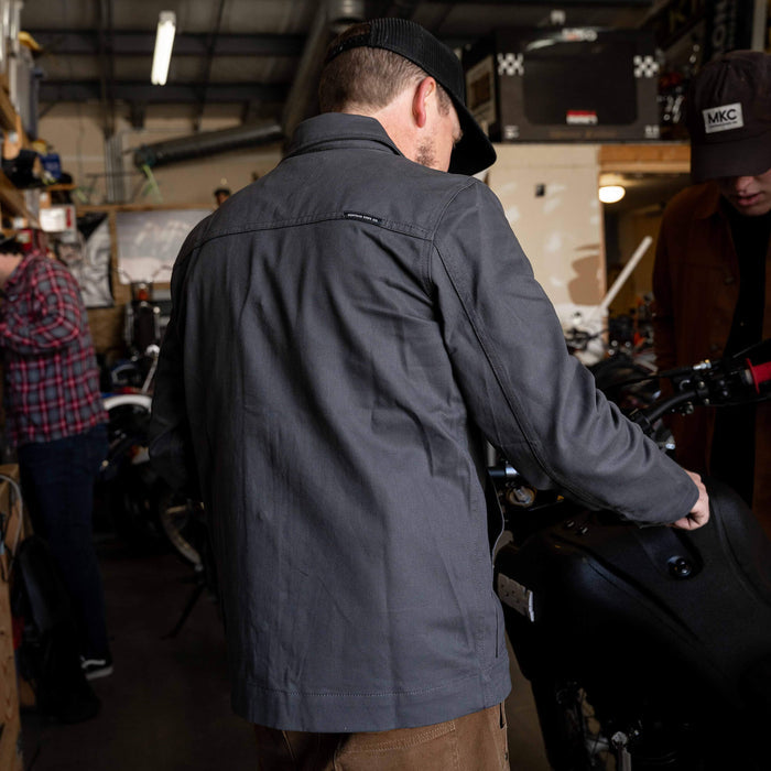 Charcoal MKC Work Jacket worn by a man in a workshop, showcasing its durable design and American craftsmanship.