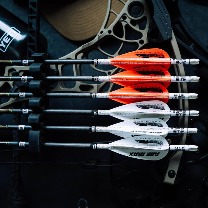 A close-up of MAX Stealth Arrow Vanes in orange, white, and black, arranged on arrows against a bow backdrop.
