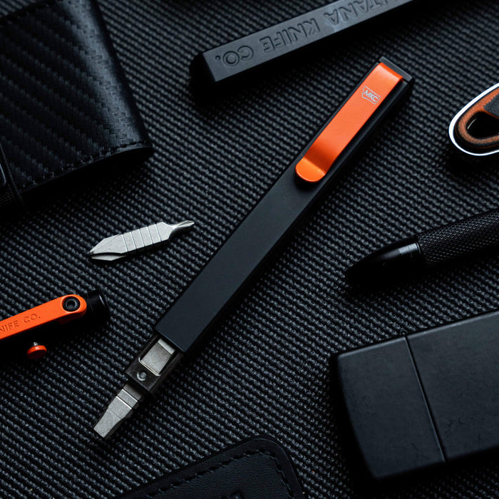 MKC X BIG IDEA DESIGN BIT BAR INLINE MAX, a sleek black multi-tool with an orange clip, surrounded by various tools and accessories.