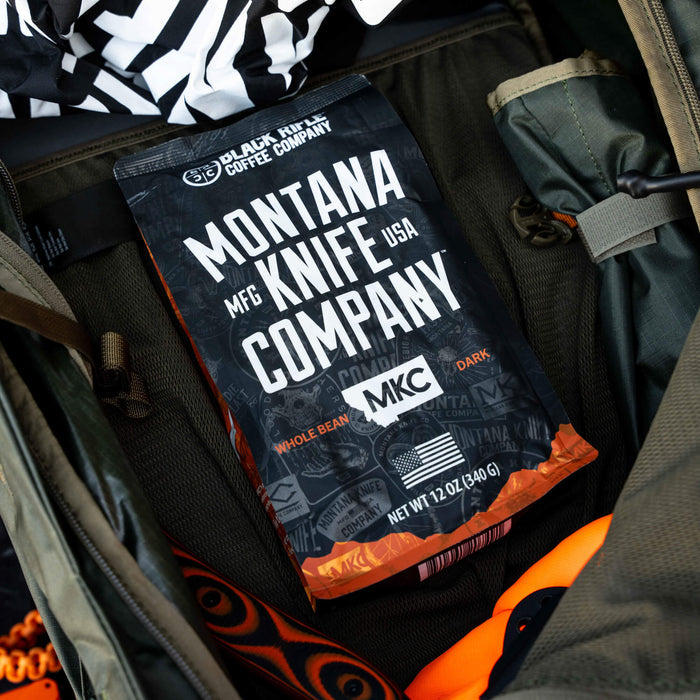 Whole bean coffee bag featuring MKC and BRCC branding, nestled in an outdoor gear bag, showcasing rugged lifestyle appeal.