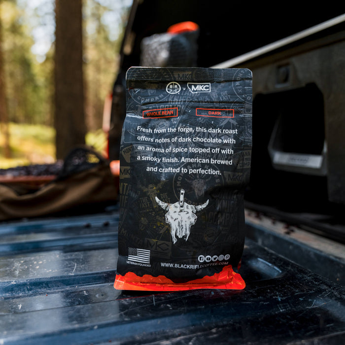 Whole bean coffee bag featuring MKC X BRCC Signature Dark Roast with a smoky finish and chocolate notes, set on a truck bed.
