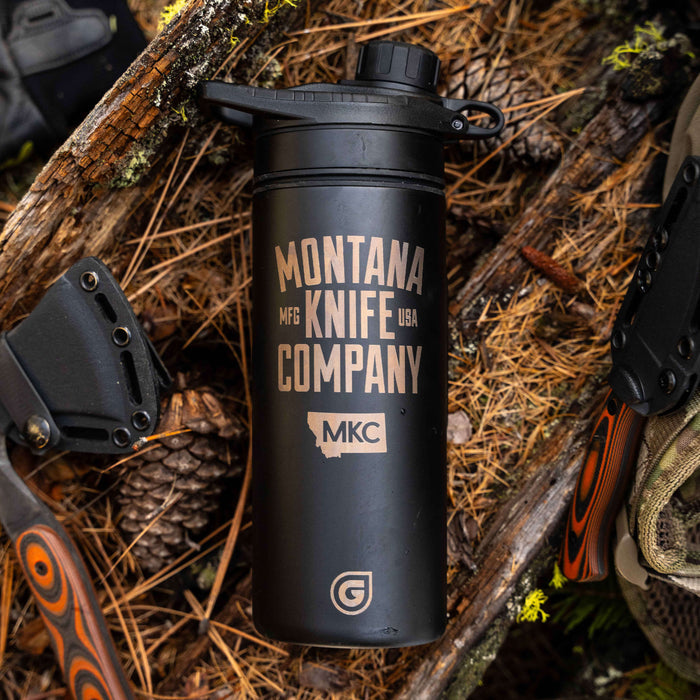 Black 24oz Geopress Ti purifier by MKC and GRAYL, featuring the Montana Knife Company logo, set on a rustic wooden background.