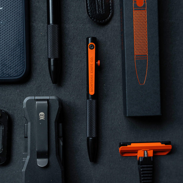 Montana Knife Company EDC Mini Pen in black with orange accents, surrounded by various tools and accessories.