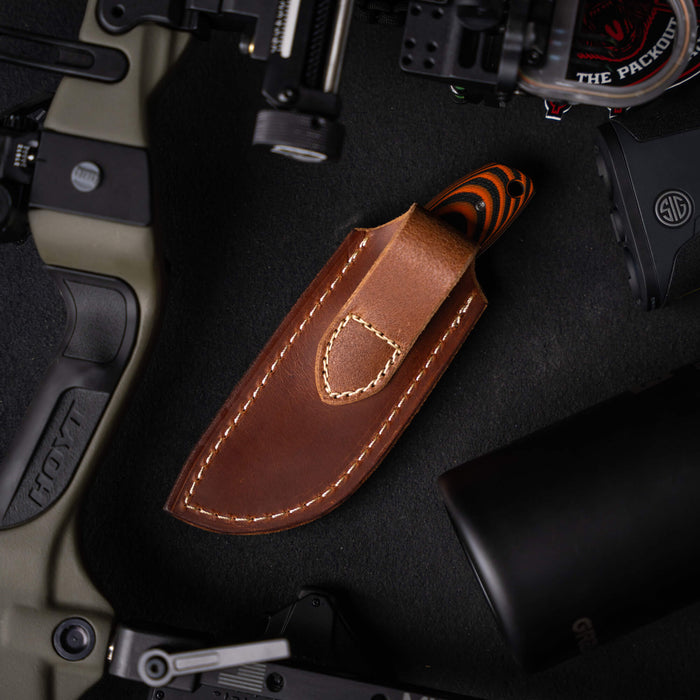Vertical leather sheath for knives, featuring a brown finish and stitched detailing, surrounded by tactical gear.