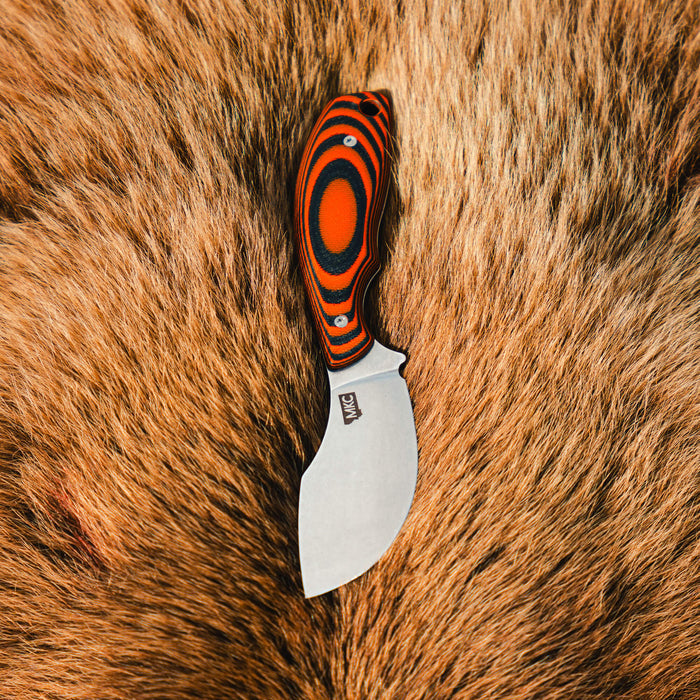 Orange and black PACKOUT SKINNER knife with a curved blade, resting on a textured fur background.
