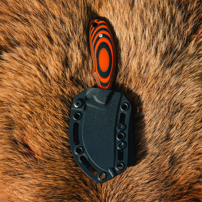 Orange and black PACKOUT SKINNER knife on fur background, featuring a durable handle and sleek design for outdoor use.