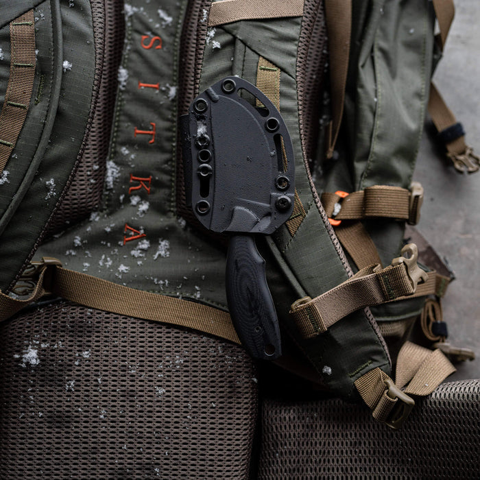 Montana Knife Company's PACKOUT SKINNER in black PVD, secured to a rugged backpack, ideal for outdoor use.